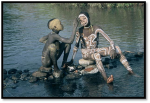 this is an image of two indigenous people who are using water and clay to paint designs on each other's bodies.