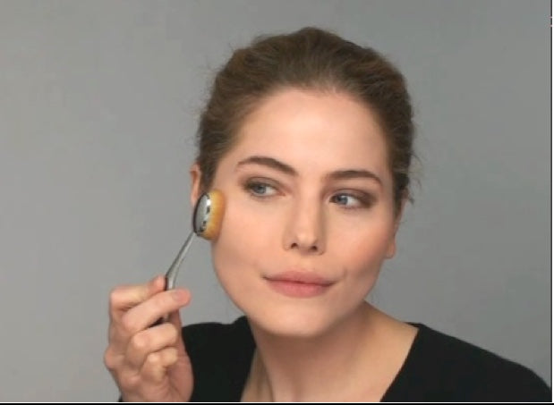 this is an image of a model holding the Elite Oval 7 brush to apply blush or foundation to her cheek area.