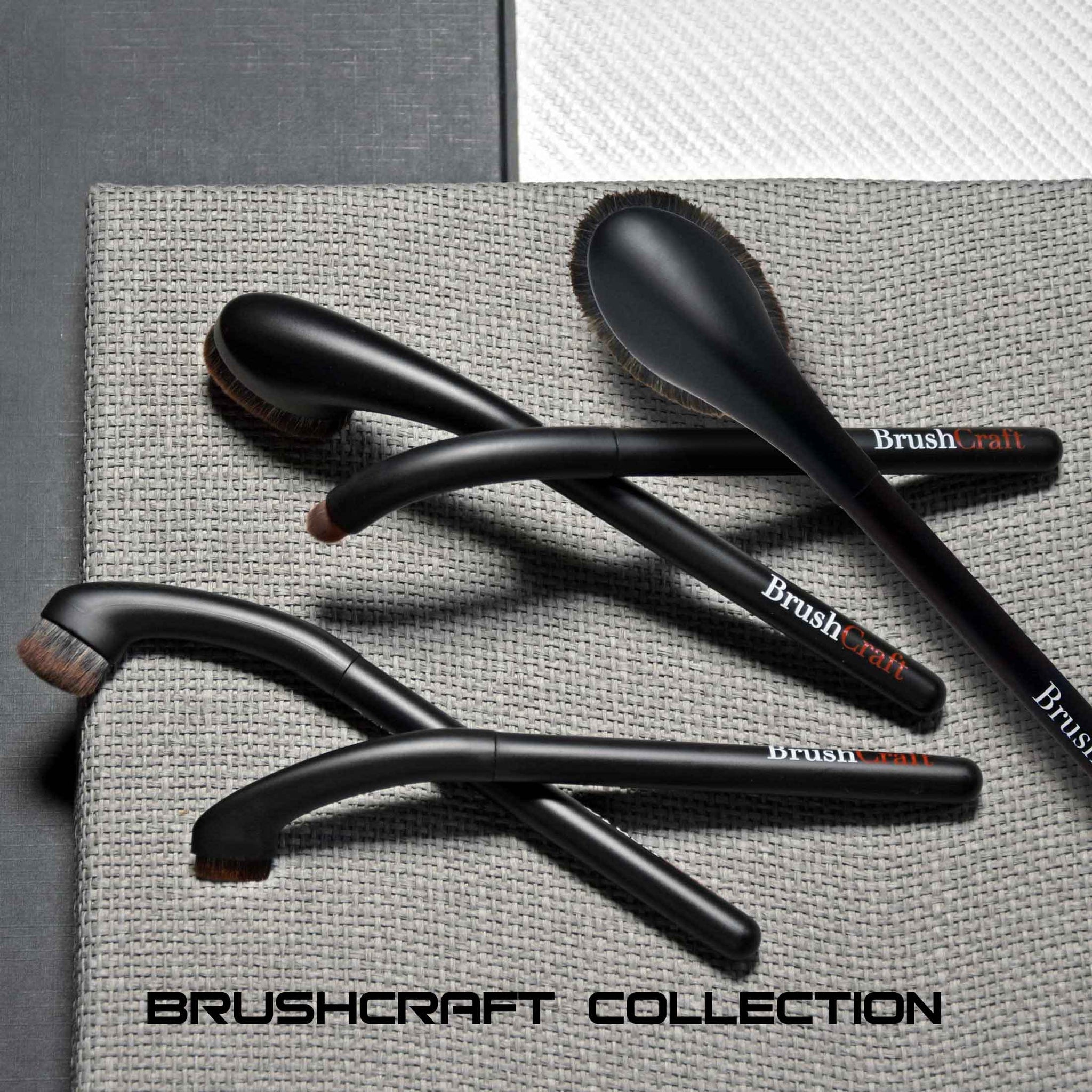 several BrushCraft brushes arranged on a loose woven fabric surface with rectangular layers of materials underneath. clicking on this image will take you to the BrushCraft Collection products listing